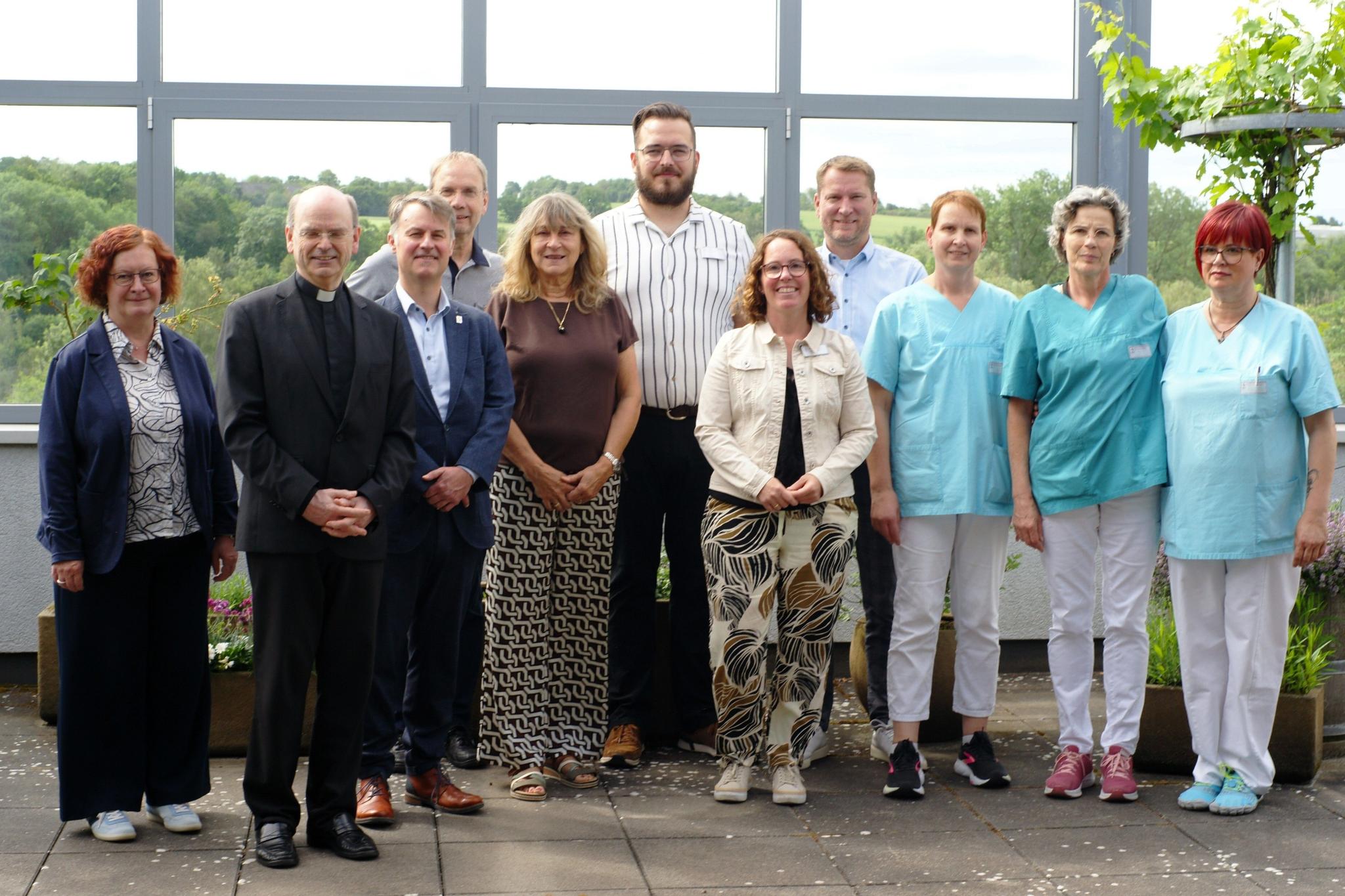 Ein Gruppenfoto, auf dem auch Menschen in hellblauer Pflegekleidung zu sehen sind.