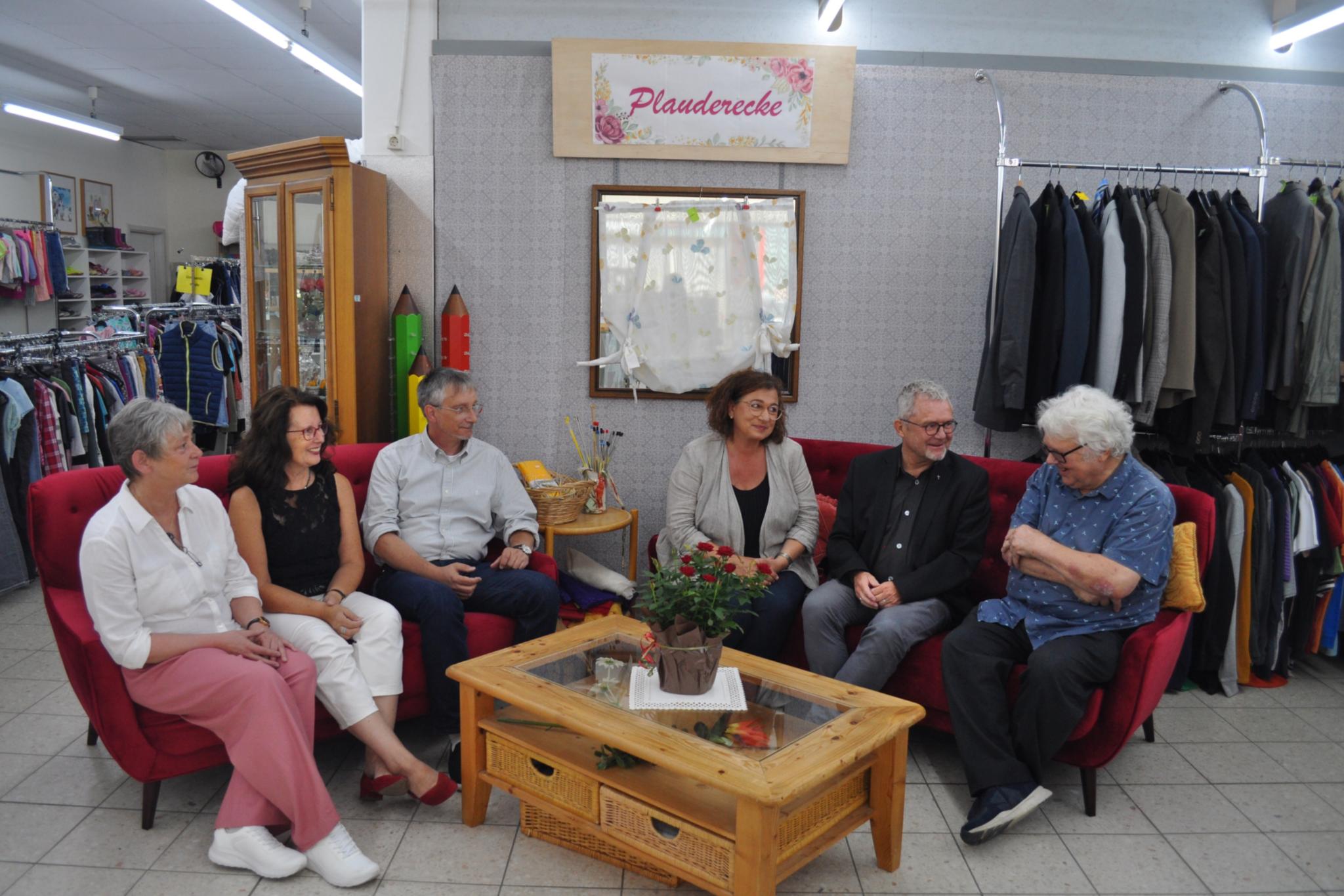 Menschen sitzen an einem  Tisch im Kleiderladen und sprechen miteinander
